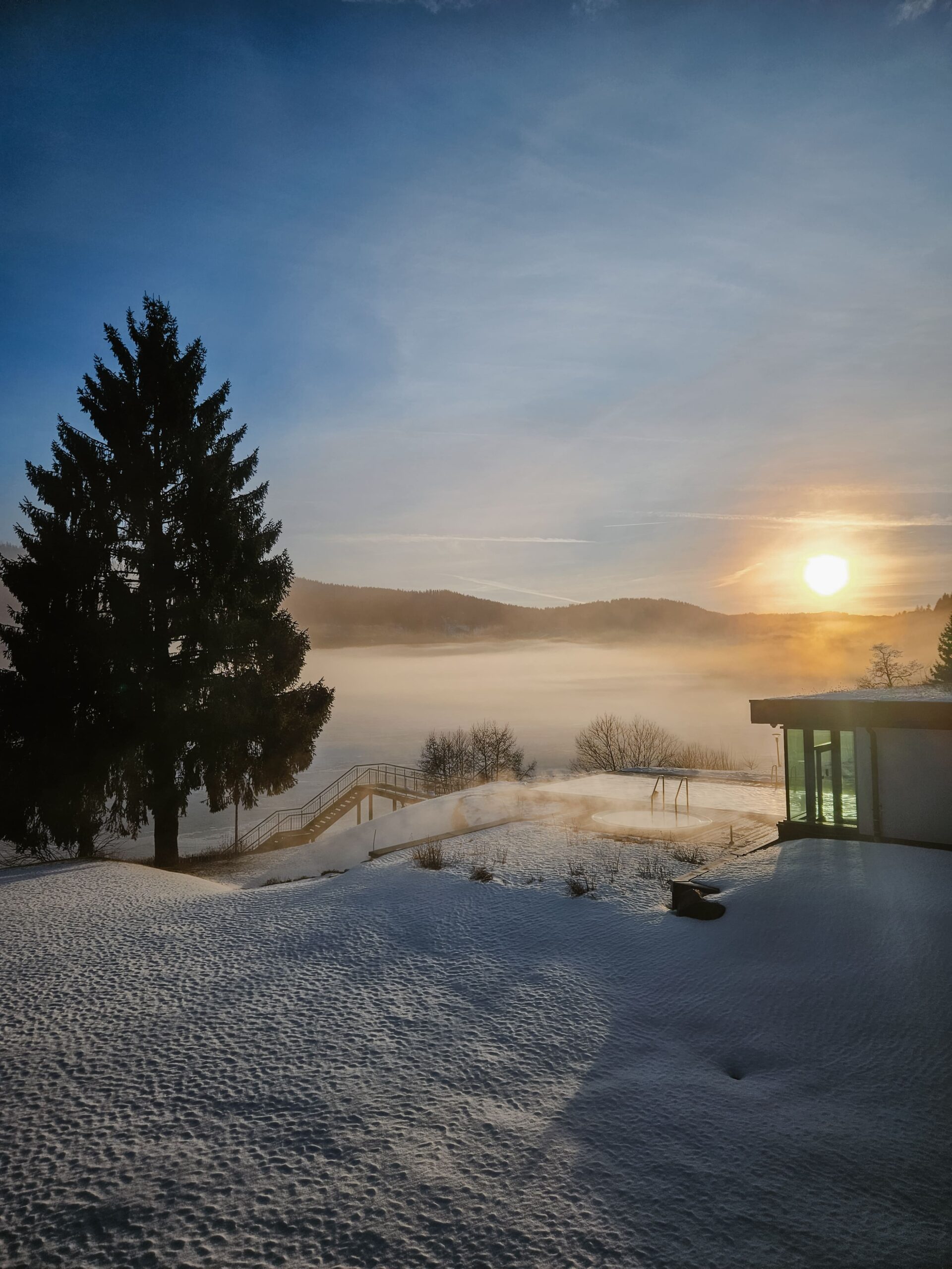 Winterlandschaft am See bei Sonnenaufgang, Blick auf Außen Pool & außen Whirlpool am verschneiten Ufer, ruhiger See, schöne Abendstimmung.