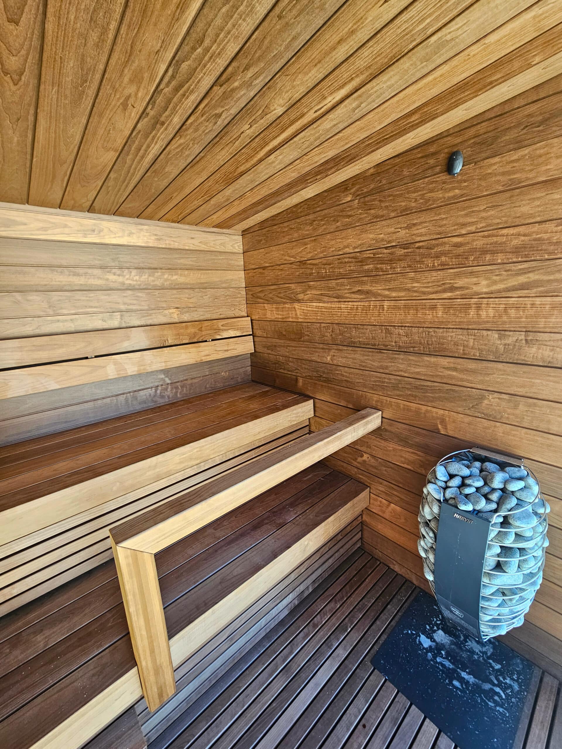 Innenraum Pop-up Sauna am Strand des Seehotel Wiesler, einer modernen Holzsauna mit zweistufigen Sitzbänken und Saunaofen mit Steinen vorne rechts.